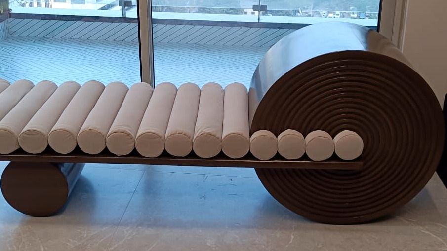 Daybed with row of ivory bolster cushions and a coiled timber terminal.