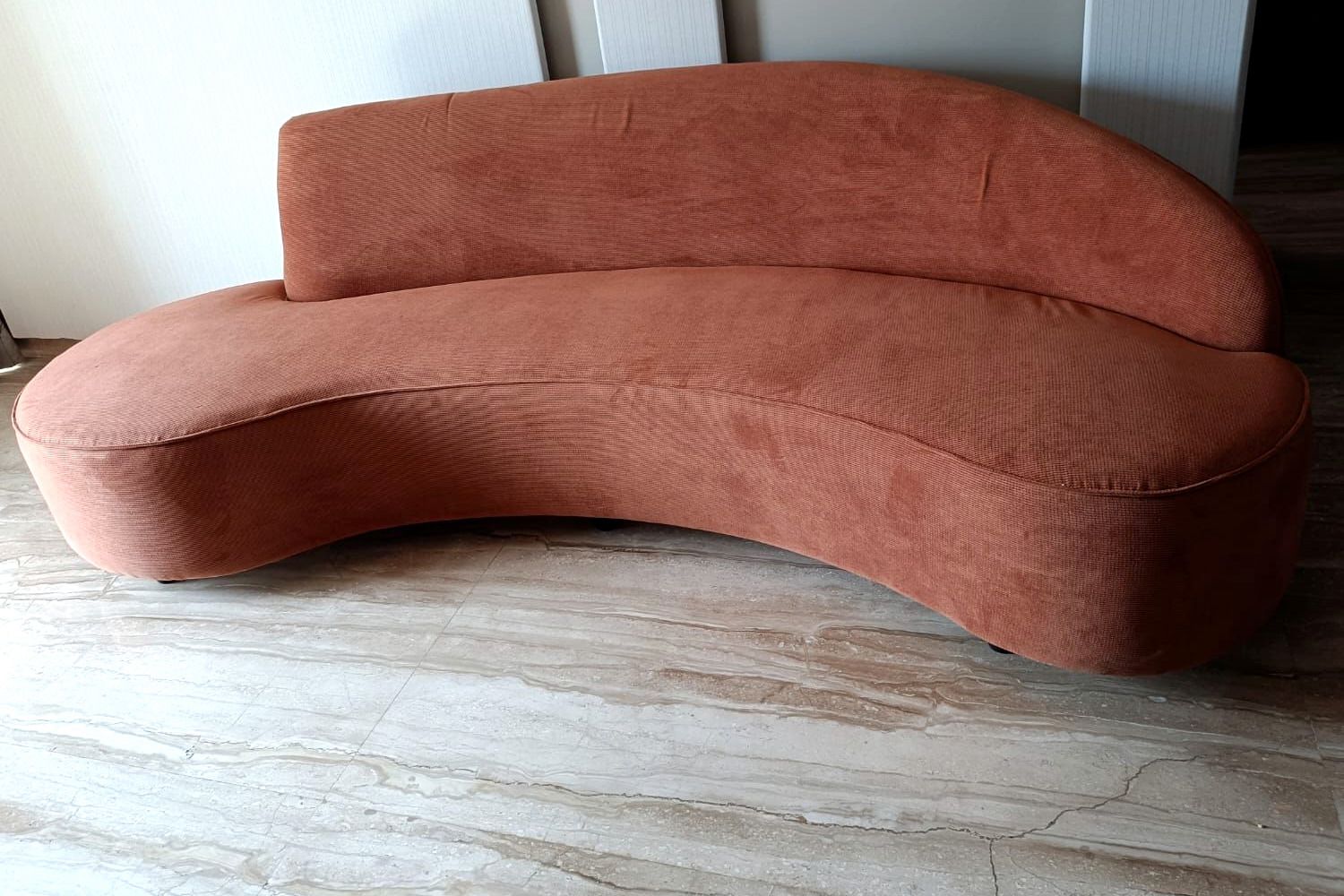 Curved rust-coloured sofa on a travertine floor.